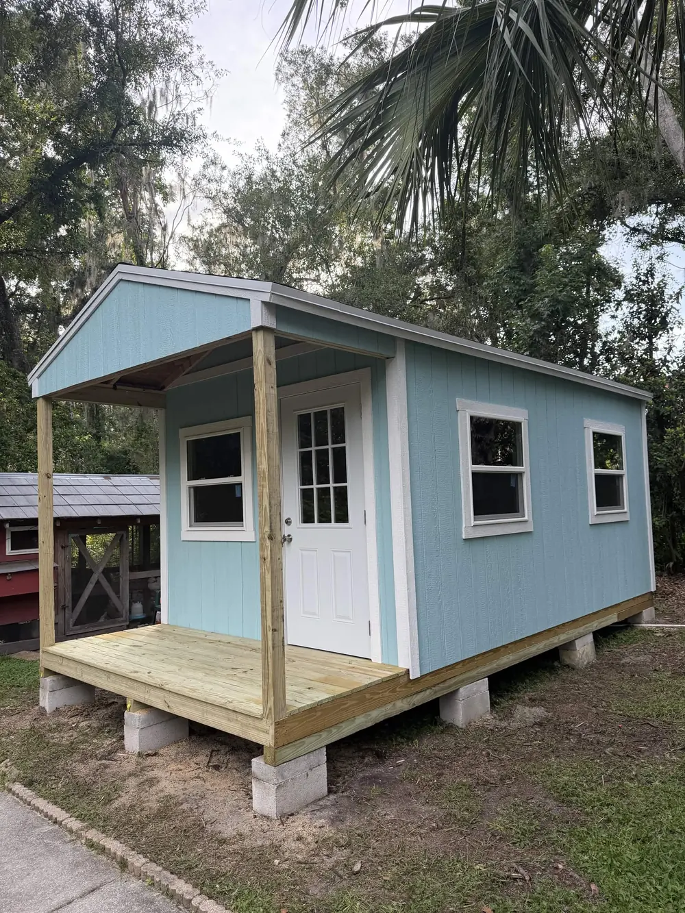 Blue custom shed with a covered porch and two windows