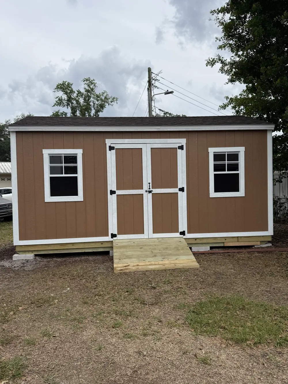 Wide tan storage shed with double doors and two windows